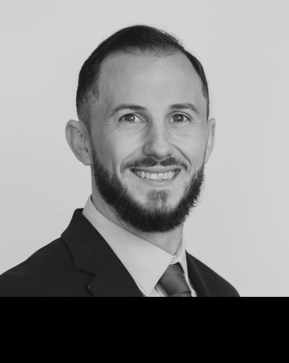 Black-and-white headshot of a man named JT Hopple with a beard, wearing a suit and tie, smiling.