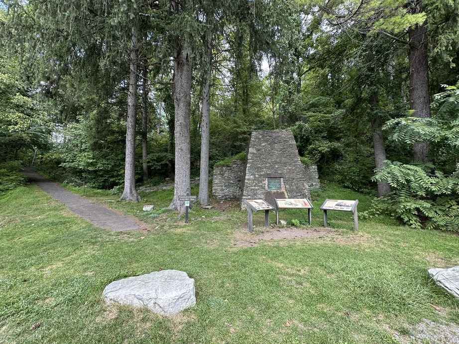 Historic stone furnace called the Caledonia surrounded by dense trees in Franklin County, Pennsylvania, with informational plaques on display.