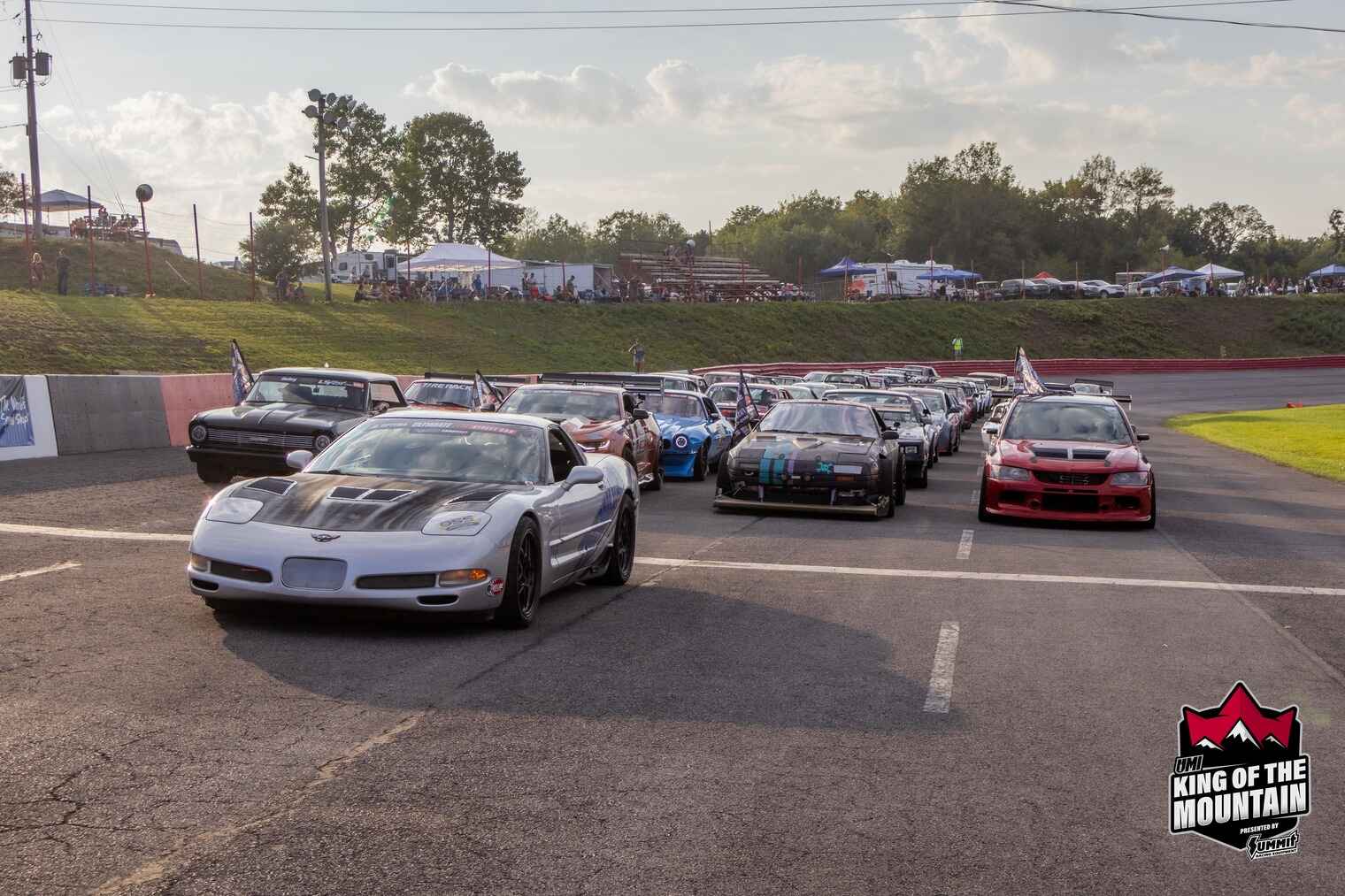 A lineup of performance cars on the starting grid at a racetrack in Clearfield County, with spectators and grassy hills in the background.