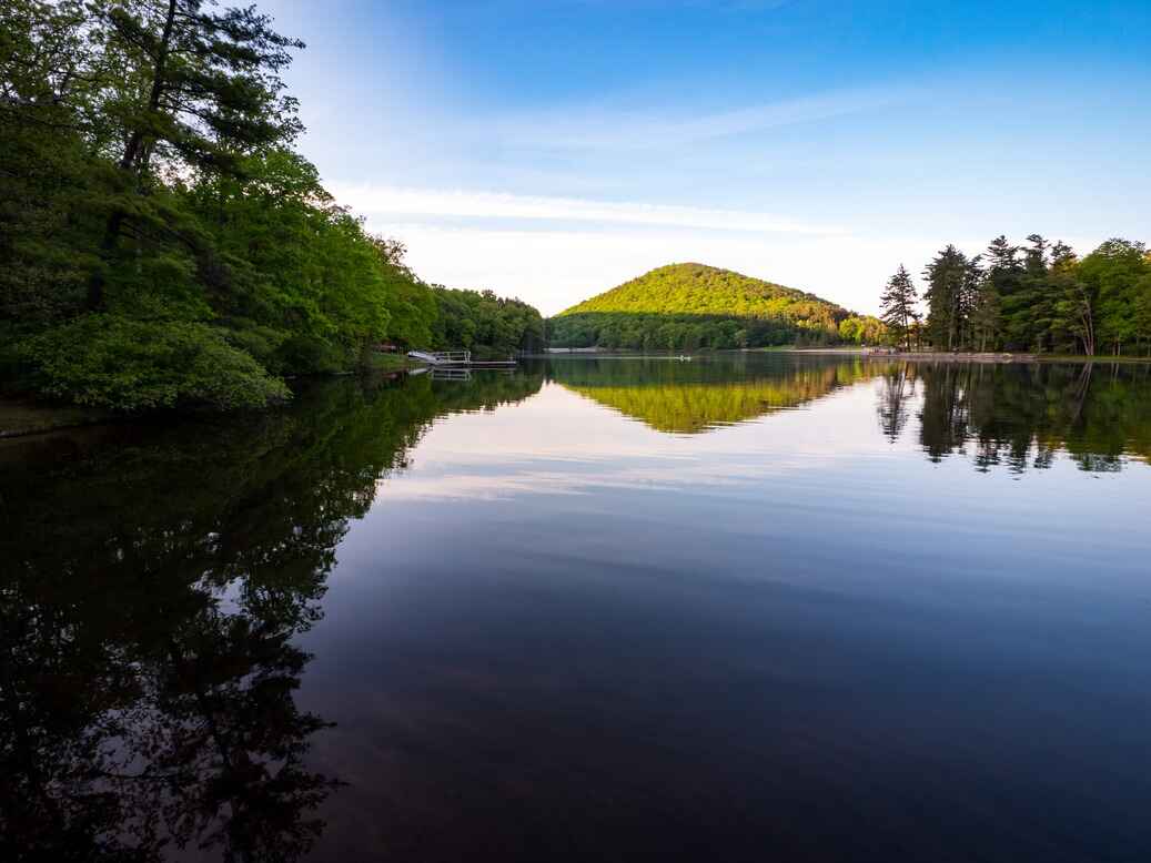 A calm lake reflecting the surrounding trees and a distant green hill in Cowans Gap State Park, located in Fulton County, Pennsylvania.
