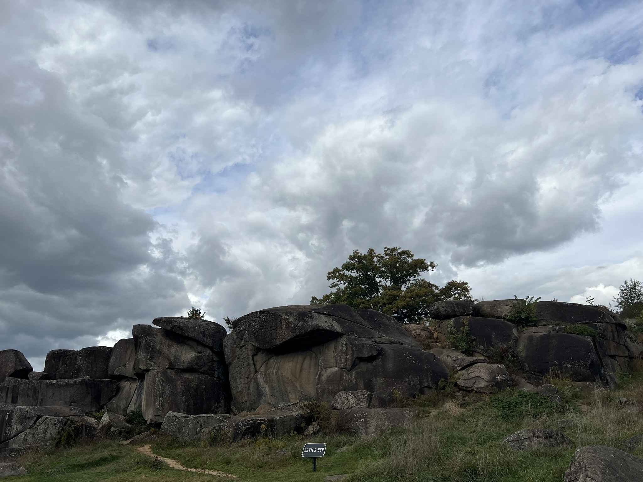 Rock formations at Devil's Den in Gettysburg, surrounded by grass and a cloudy sky above.