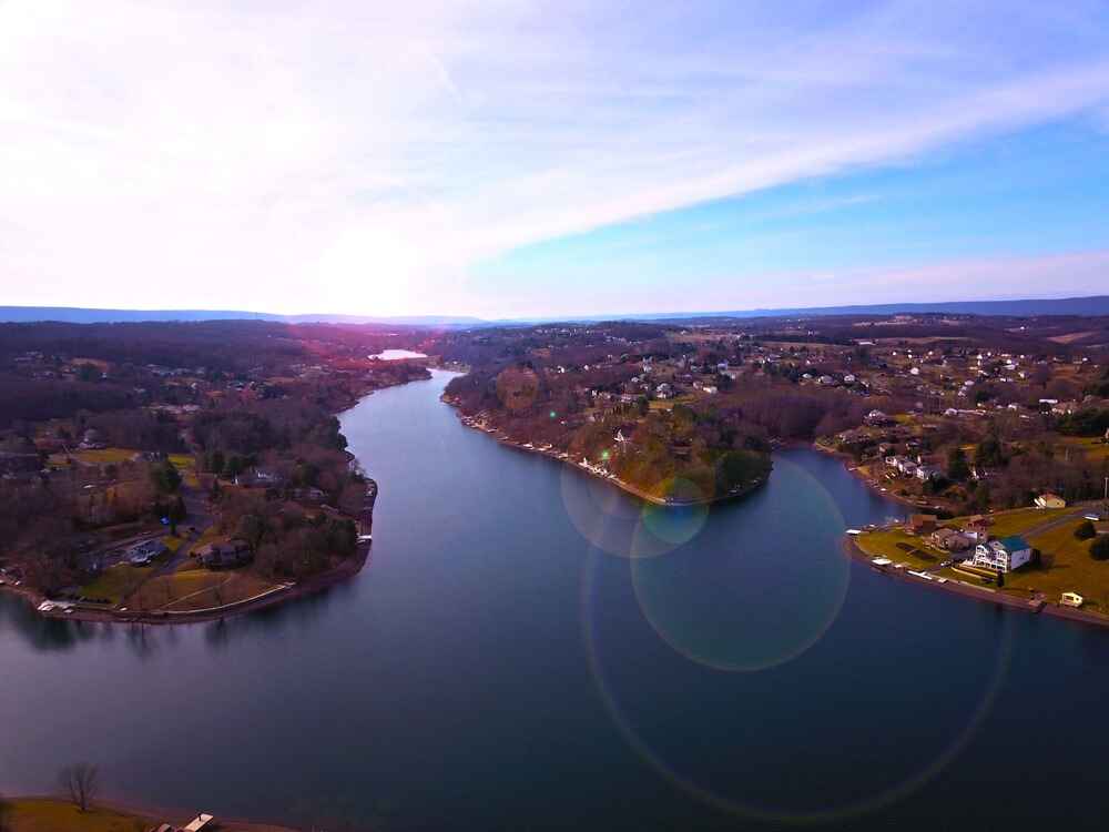 An aerial view of Lake Wynonah, Schuylkill County, with a winding body of water surrounded by residential homes and rolling hills under a clear sky.