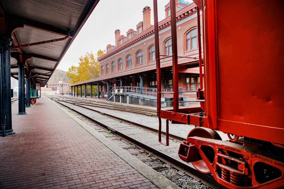 A historic red-brick railroad station in Cumberland, MD, with a vintage train car on the tracks.