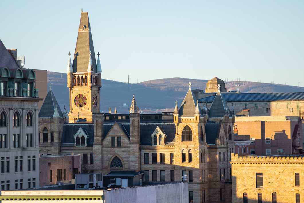 The Scranton Municipal Building in Lackawanna County, Pennsylvania, stands with Gothic-style architecture and a towering clock spire, with distant mountains in the background.