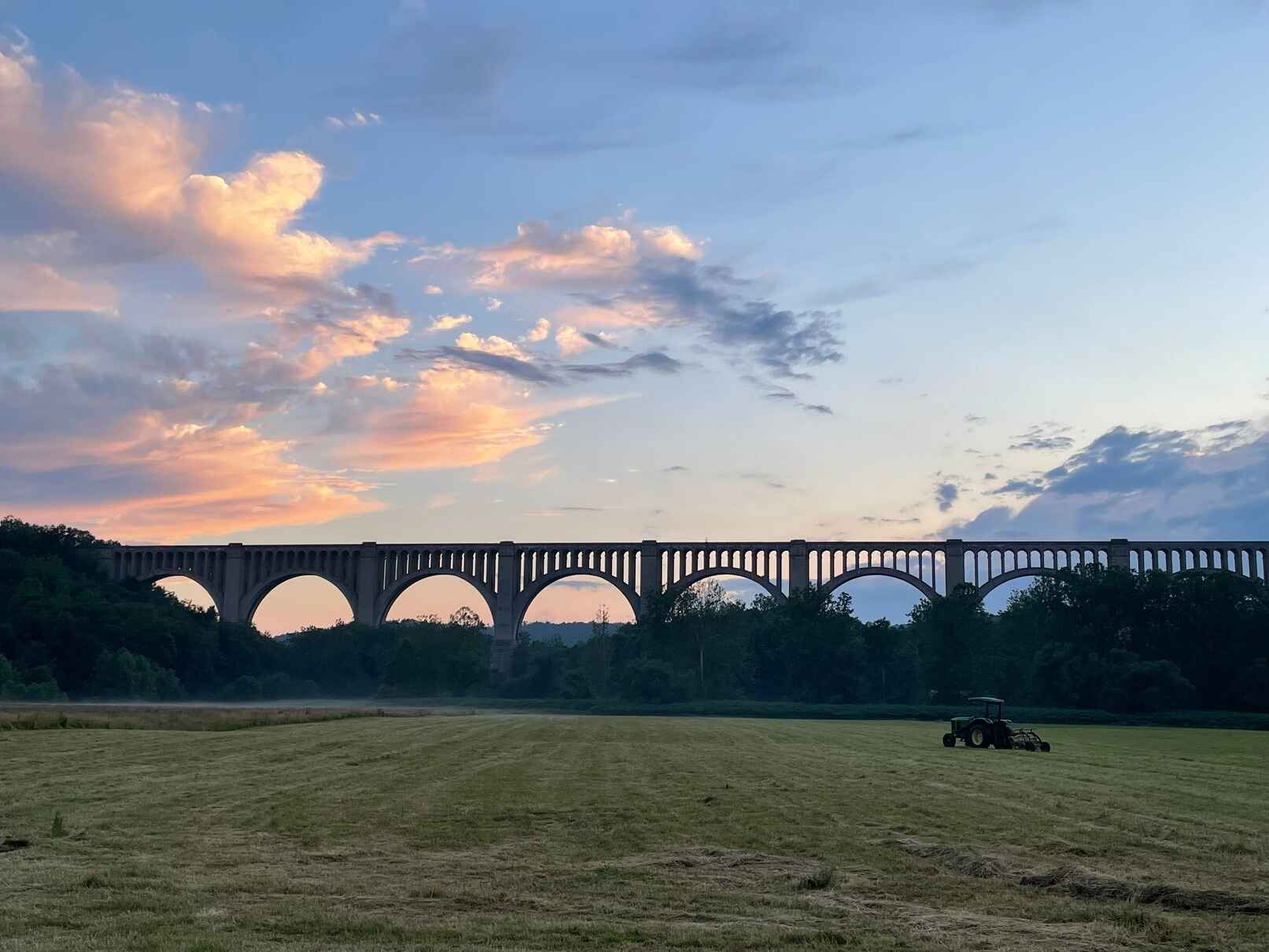 Sunset over the Tunkhannock Creek Viaduct in Wyoming County, PA, with a tractor in a freshly mowed field.