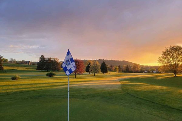 The scenic Berwick Golf Club in Columbia County, with a golf course flag and lush greenery illuminated by a vibrant sunset.