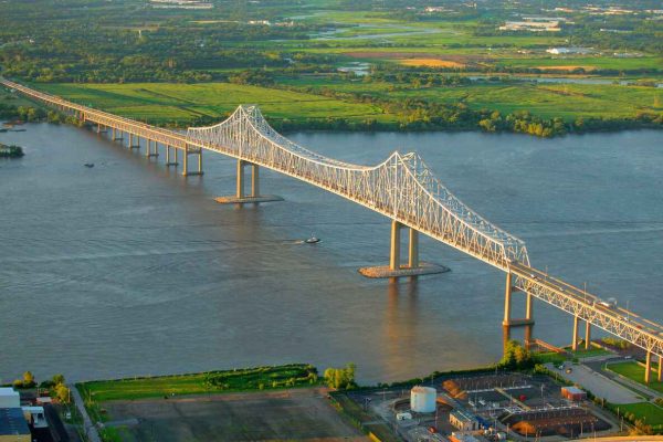 The Commodore Barry Bridge stretches across the Delaware River, connecting Pennsylvania and New Jersey, with a backdrop of green farmland and water in Delaware County.