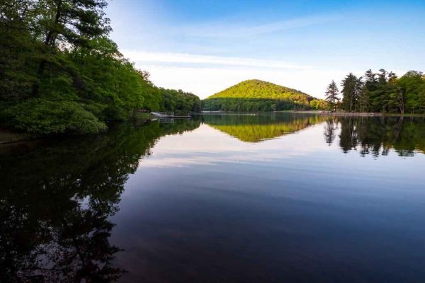 A calm lake reflecting the surrounding trees and a distant green hill in Cowans Gap State Park, located in Fulton County, Pennsylvania.