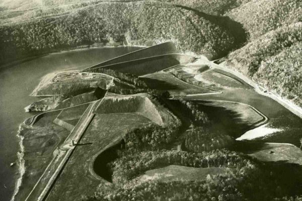 Black-and-white aerial photograph of Raystown Lake Dam in Huntingdon County, Pennsylvania, showing the large dam structure, winding waterways, and surrounding forested landscape.