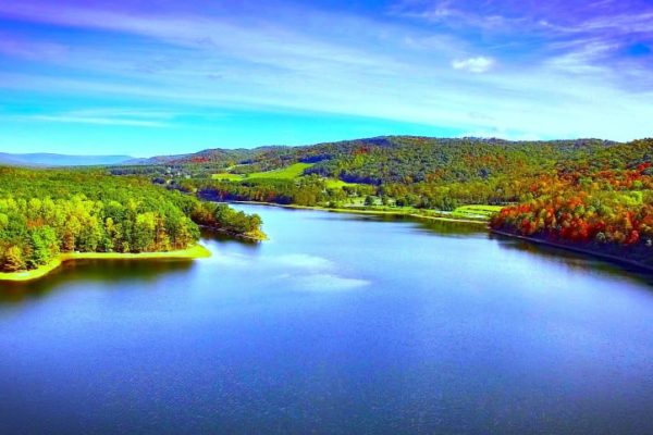 A vivid blue lake stretches between rolling green mountains under a bright blue sky at Rocky Gap State Park, Maryland.