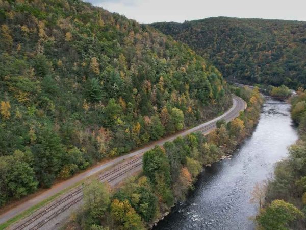 A railway winds through the lush, tree-covered hills of Lehigh Valley Gorge in Schuylkill County, Pennsylvania, alongside a flowing river.
