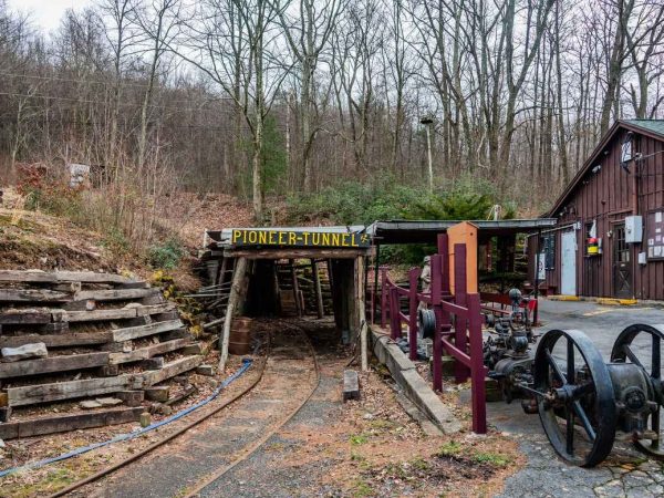 The entrance to the Pioneer Tunnel Coal Mine in Schuylkill County, Pennsylvania, features wooden beams and historic mining equipment, surrounded by bare trees.